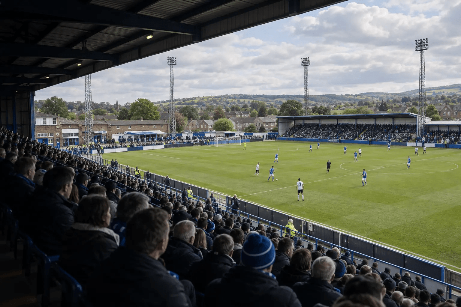 A busy match at a community football ground in daylight